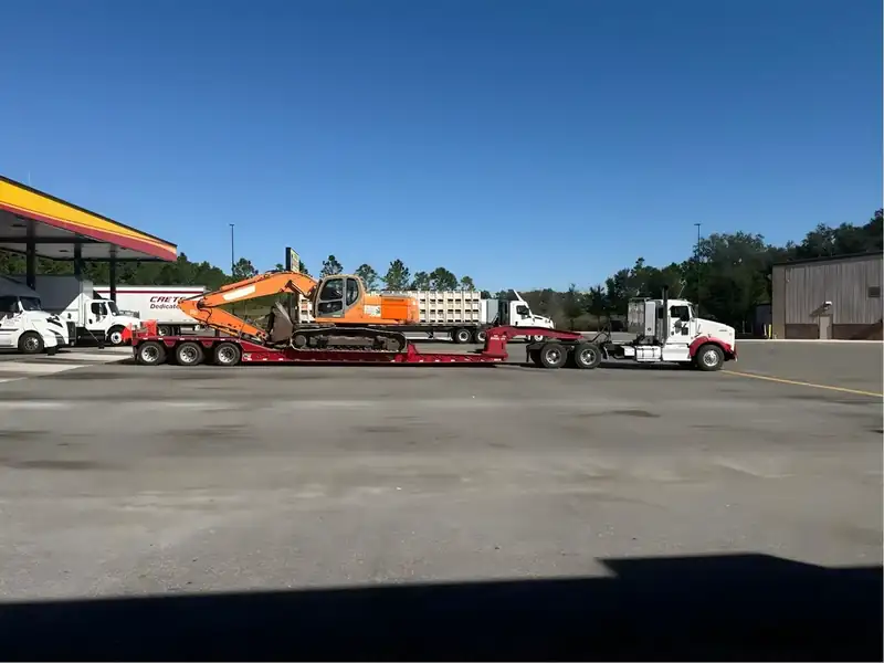Orange excavator on a lowboy trailer behind a Kenworth tractor