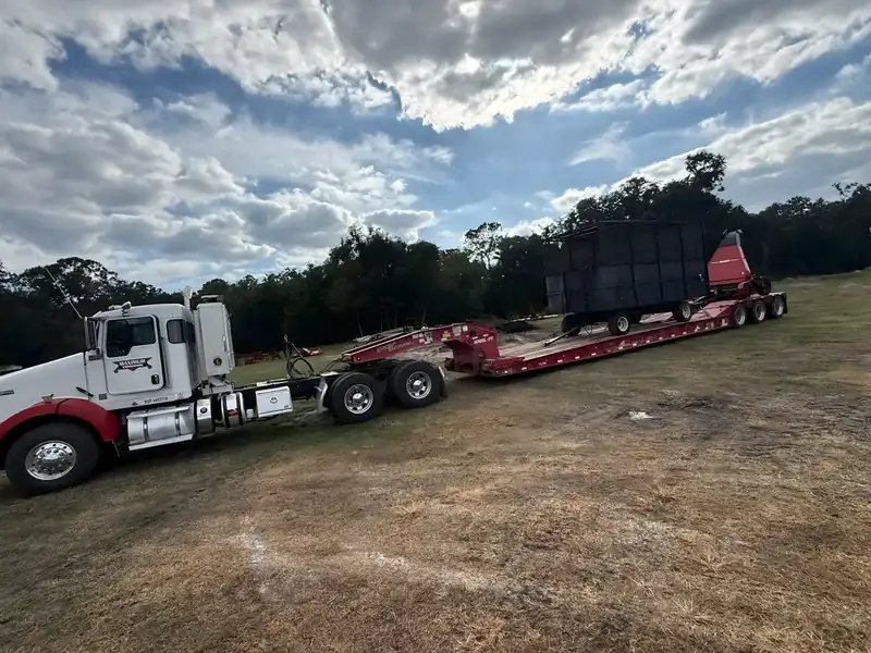 Farm equipment loaded on a trailer behind a white Kenworth tractor