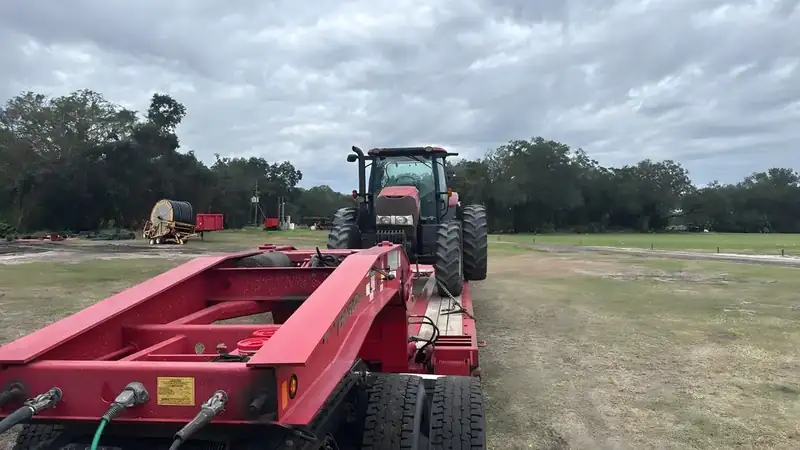 Red tractor on the deck of a red lowboy trailer